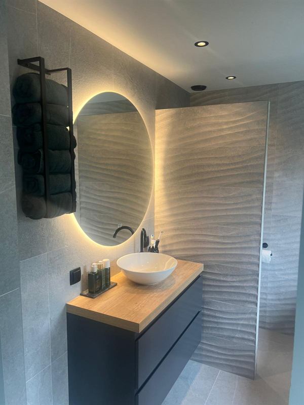 Badkamer met ronde spiegel en houten wastafelmeubel